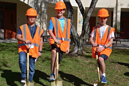 3 SWPPP interns posing in bright orange vests with shovels preparing for the start of the DROPS funded project at their school